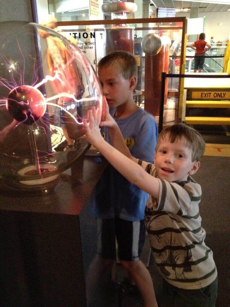 Two boys touching glowing plasma ball at museum