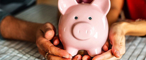 Two hands holding a pink piggy bank.