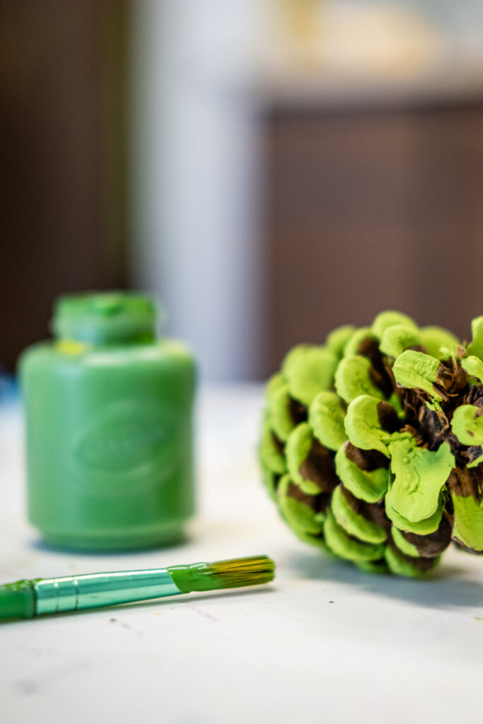 Green-painted pinecone with paint and brush.
