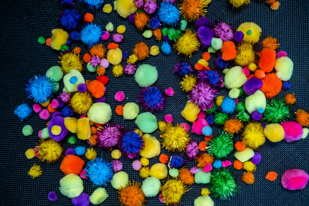 Colorful pom-poms scattered on a dark surface.