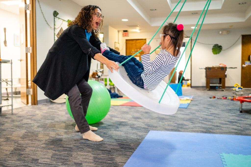A woman pulling the swing for the girl