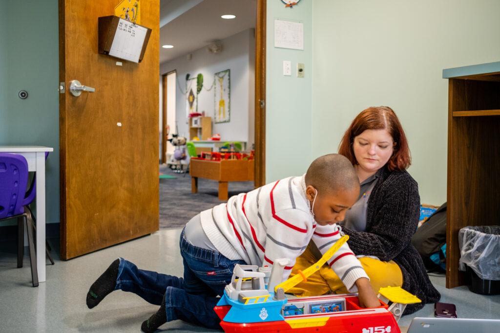 Child playing with toy boat, adult assisting.
