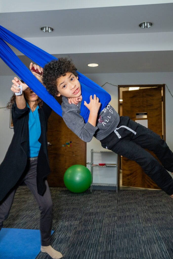 Child swinging in blue fabric harness.